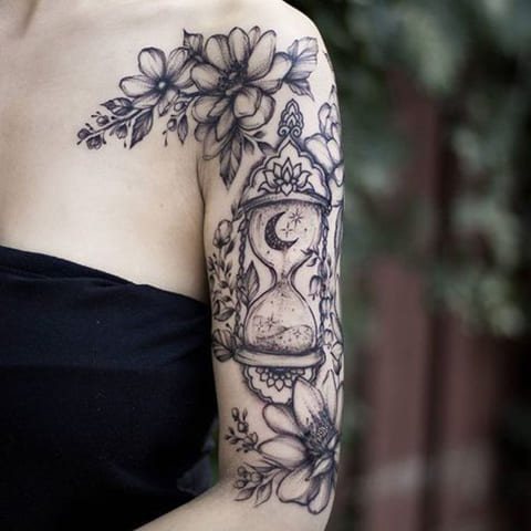 Tatuaje de reloj de arena y flores en el brazo de una chica